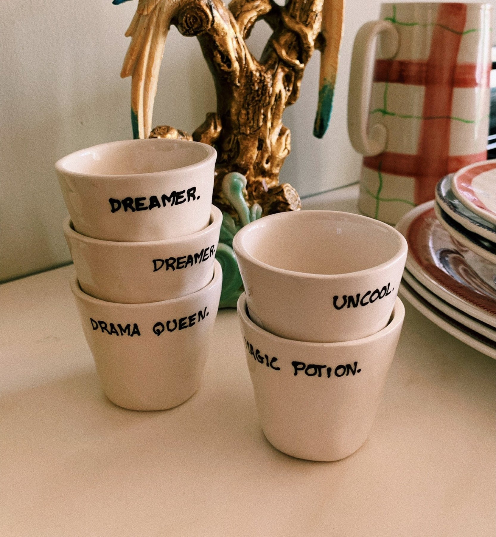 vaso de cerámica para espresso con el mensaje Drama Queen, apilado junto a otros vasos con mensajes en un ambiente lifestyle Kolorama.